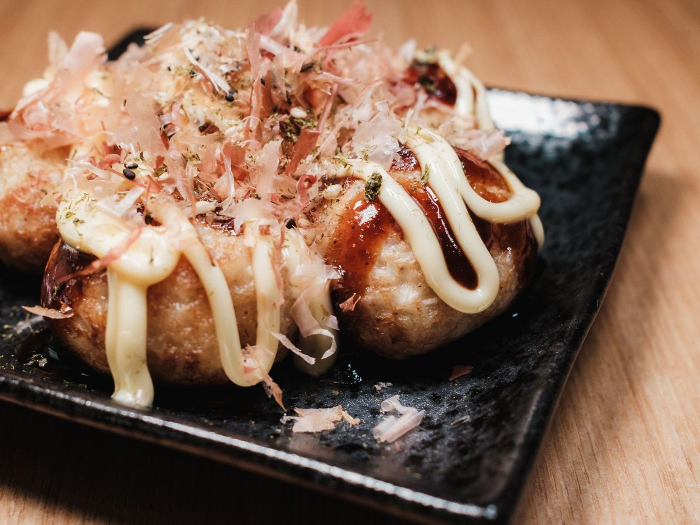 Eight takoyaki in a wooden boat tray with sauce, mayonnaise, spring onion and bonito flakes